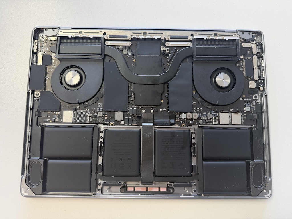 Interior of an opened MacBook Pro showing the logic board, dual cooling fans, heat pipe, and battery cells during repair at MarTech in Kennesaw, GA
